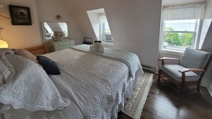 A bedroom with a large bed, a chair, a dresser, a mirror, and a window with a view. - The Scotsman Inn (Pictou)