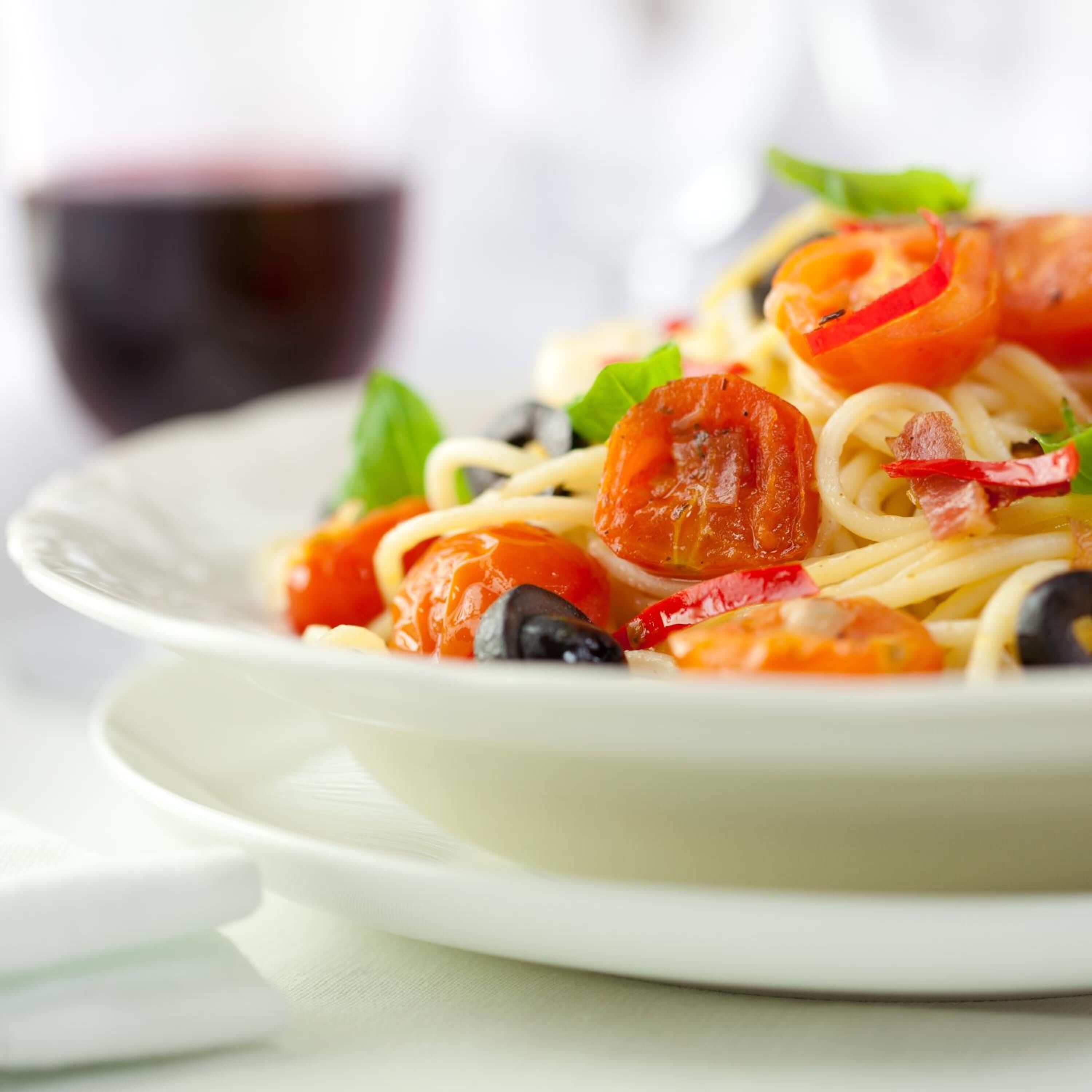 A plate of spaghetti with cherry tomatoes, black olives, and red chili peppers.