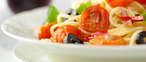 Un plato de espagueti con tomates cherry, aceitunas negras y chiles rojos.
