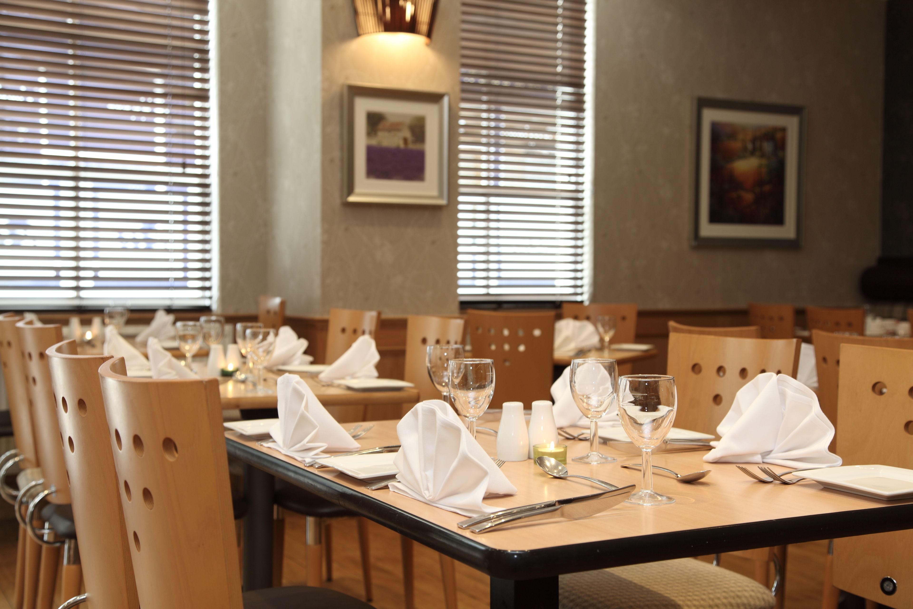 Un comedor con sillas de madera, mesas ordenadas con servilletas blancas, copas de vino y cubiertos.