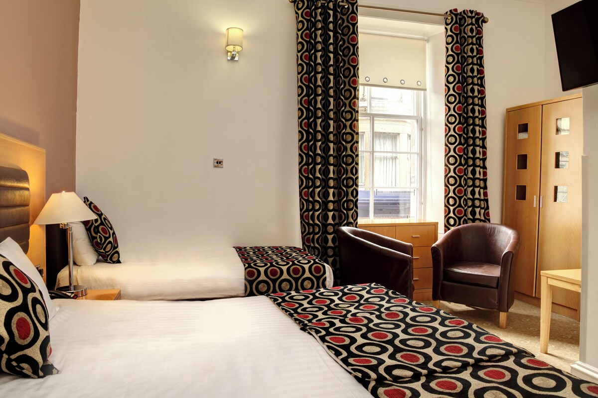 A hotel room with two beds, a desk, a chair, and a wardrobe.