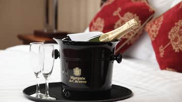 A bed with a black bucket containing a champagne bottle and two glasses on a tray.
