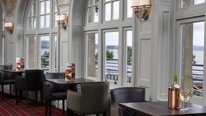 A restaurant with a red plaid carpet, tables with chairs, and a view of a body of water through large windows. - The Argyll Hotel (Dunoon)