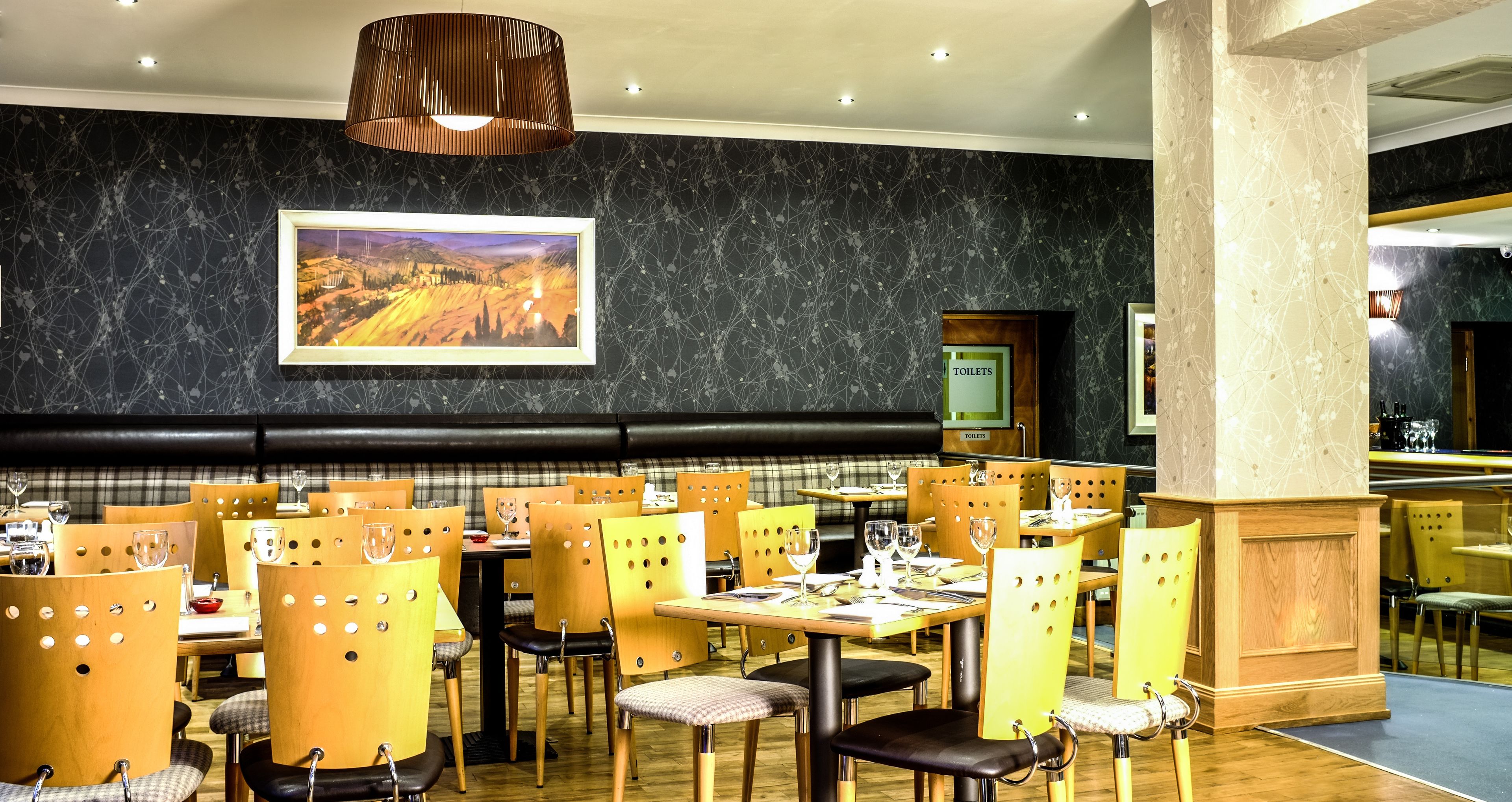 Een restaurant met houten stoelen en tafels, een zwarte marmeren wand en een lijst met een landschapschilderij.