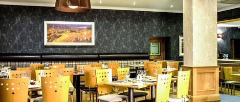 Een restaurant met houten stoelen en tafels, een zwarte marmeren wand en een lijst met een landschapschilderij.