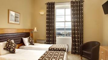 A hotel room with two beds, a chair, a desk, a lamp, and a window with curtains.
