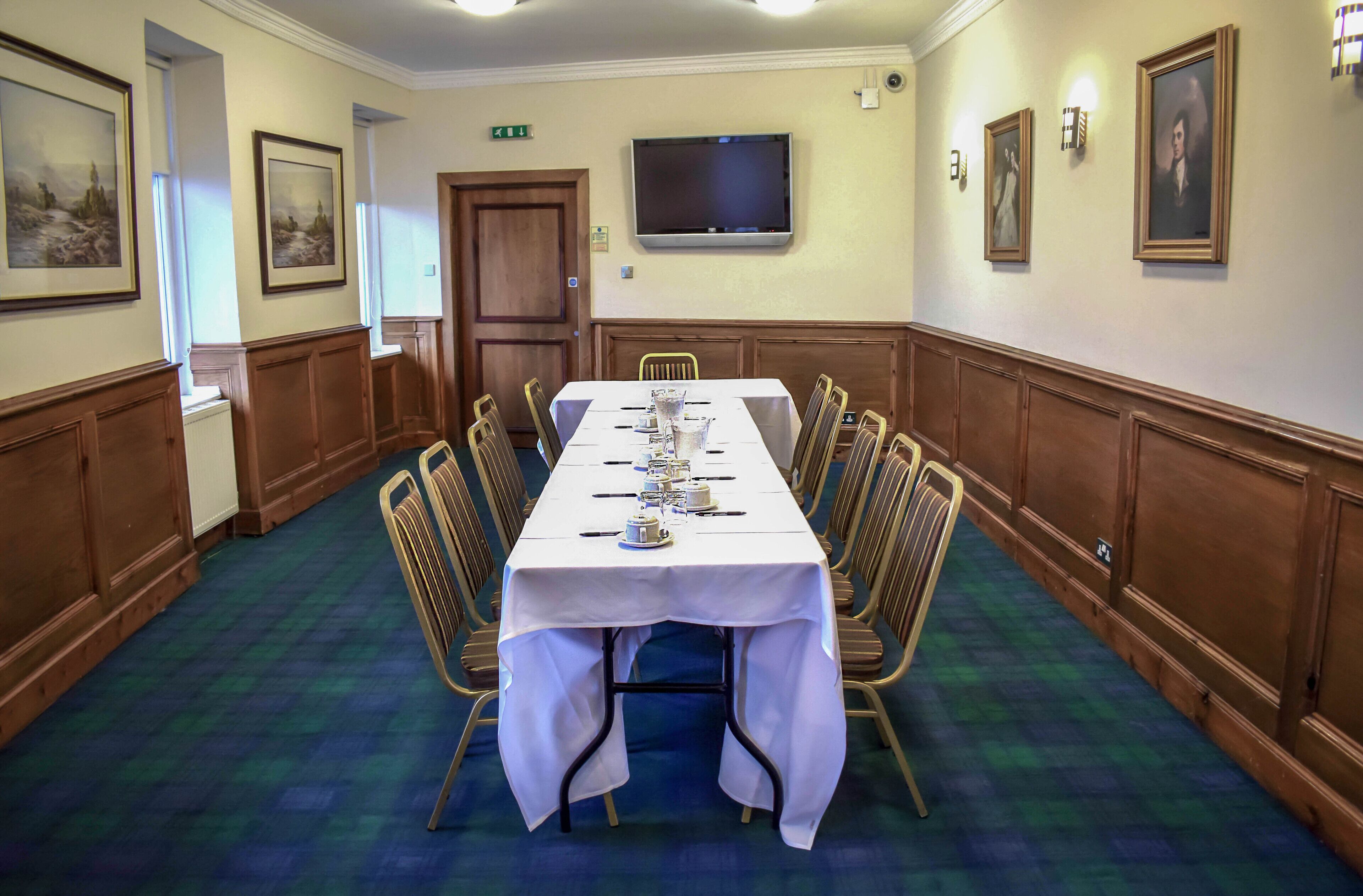 A conference room with a long table, chairs, a TV, and framed pictures on the walls.