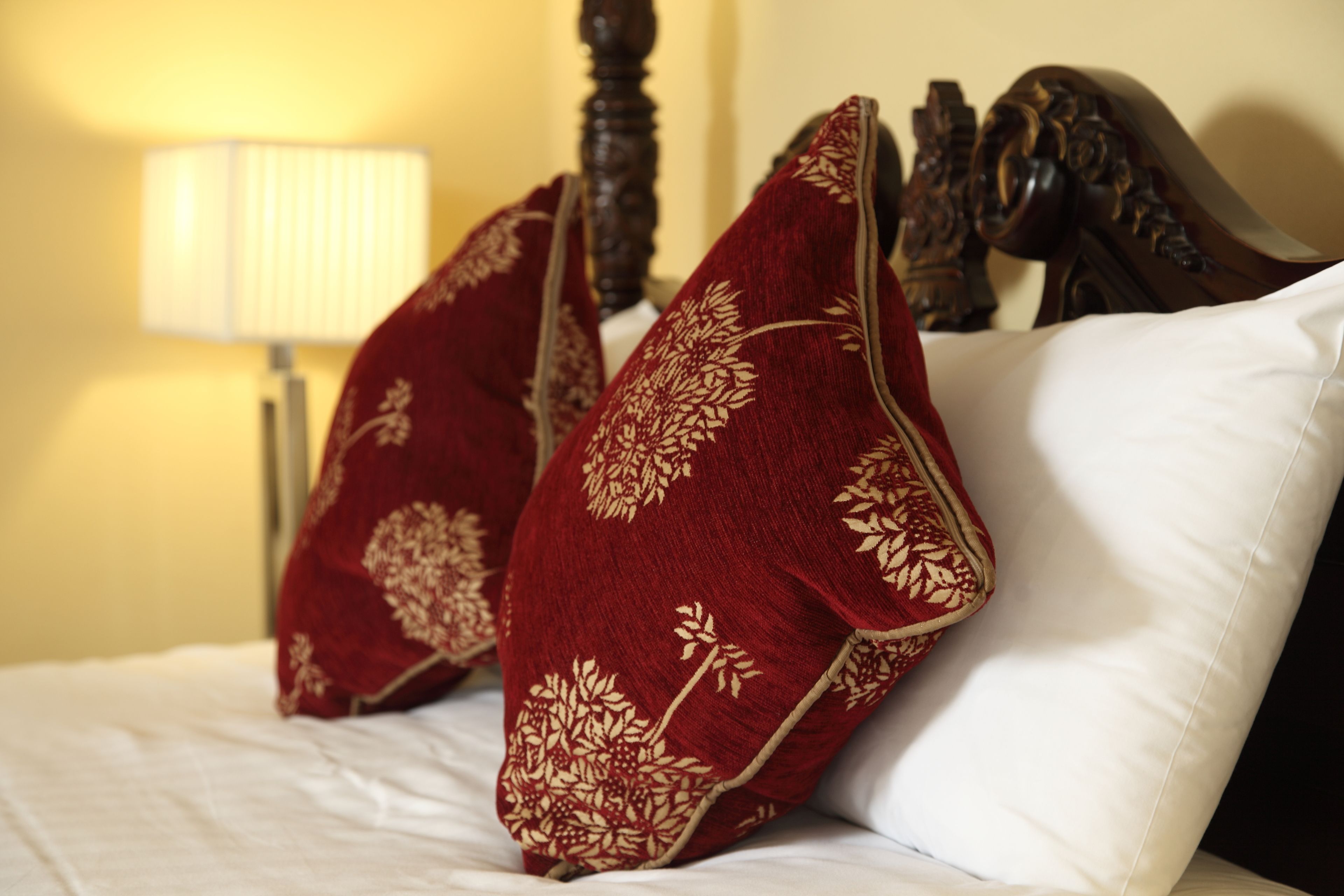 Una cama con sábanas blancas y dos almohadas rojas con motivos florales dorados.