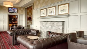 A modern lounge area with a leather sofa, a fireplace, and a bar with a variety of bottles. - The Argyll Hotel (Dunoon)