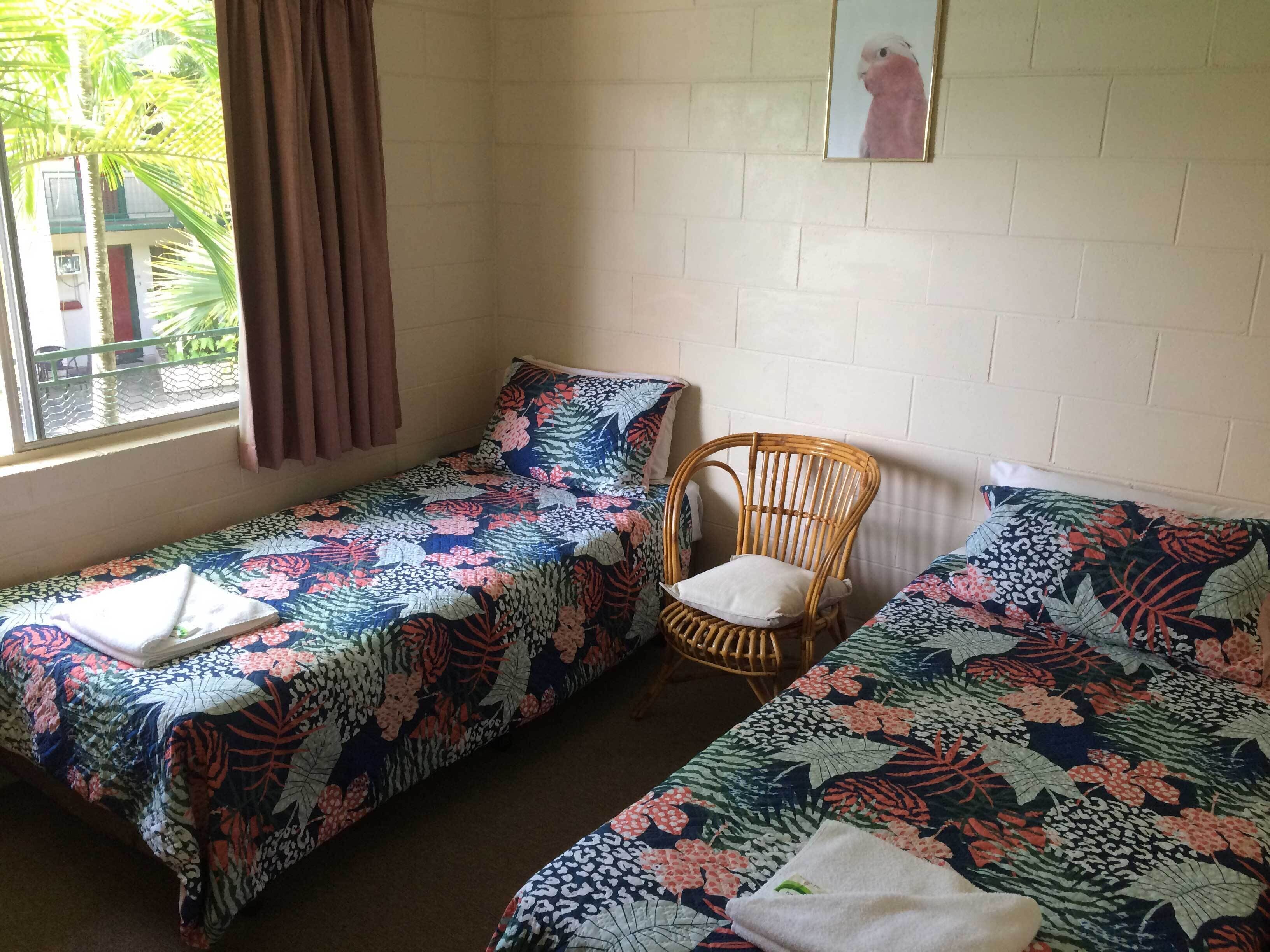 Un dormitorio con dos camas individuales, una silla de mimbre y una ventana con cortinas.