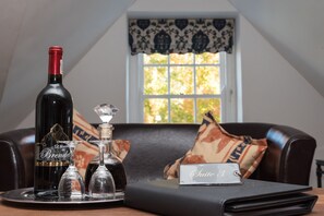 A bottle of wine, two wine glasses, and a nameplate on a tray in a room with a window and a sofa.