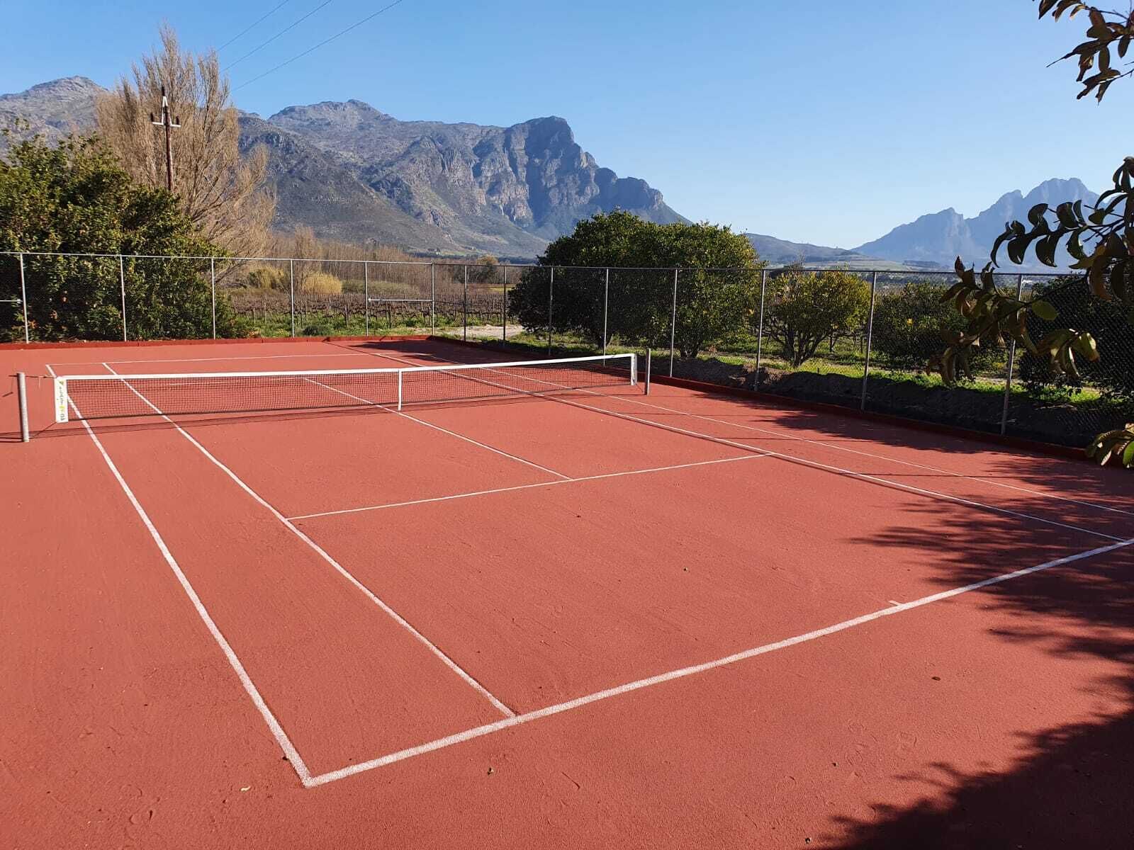 A tennis court with a net, surrounded by a fence, and mountains in the background.