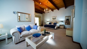 Una sala de estar con un sofá blanco, una mesa de centro, una cama con cabecera azul y un candelabro.