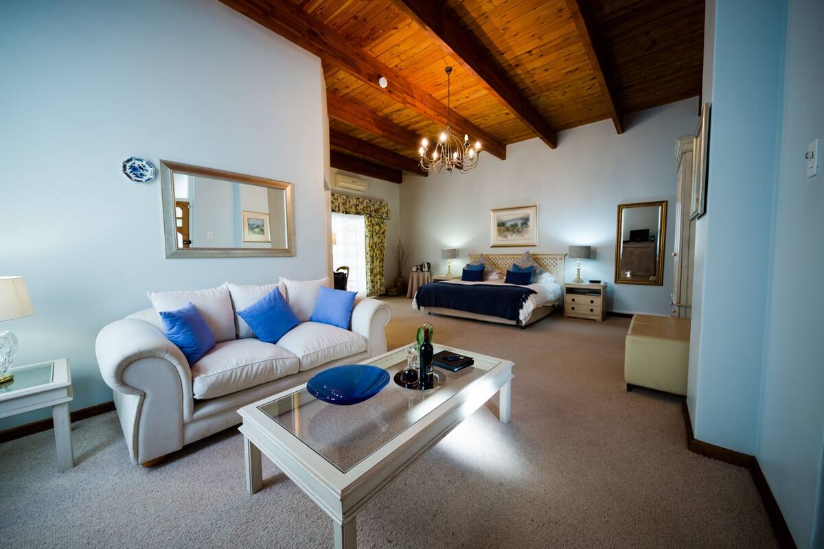 A living room with a white sofa, a coffee table, a bed with a blue headboard, and a chandelier.