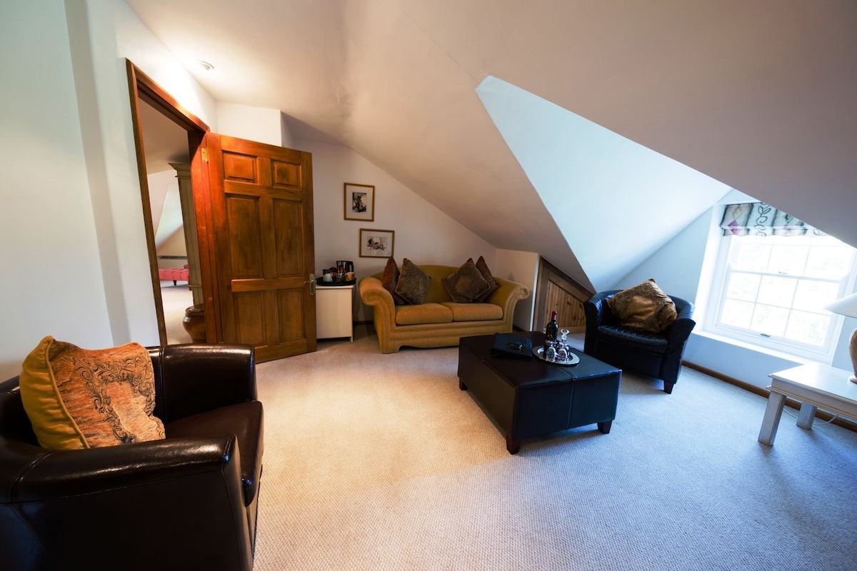 A cozy loft bedroom with a sloped ceiling, a sofa, a coffee table, and a small side table.