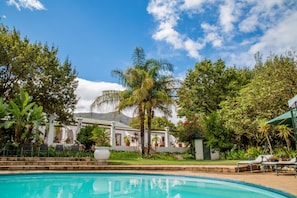 A swimming pool surrounded by lush greenery and a white building with a mountain in the background.