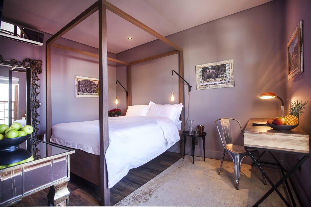 A bedroom with a four-poster bed, a desk with a chair, and a small table with fruit.