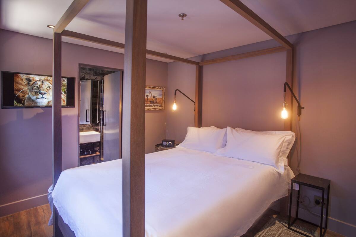 A bedroom with a four-poster bed, a television mounted on the wall, and a nightstand with a lamp.