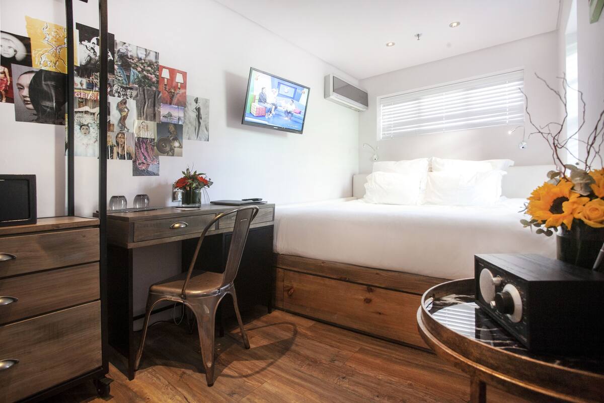 A bedroom with a bed, a desk with a chair, a TV, and a wall with pictures.