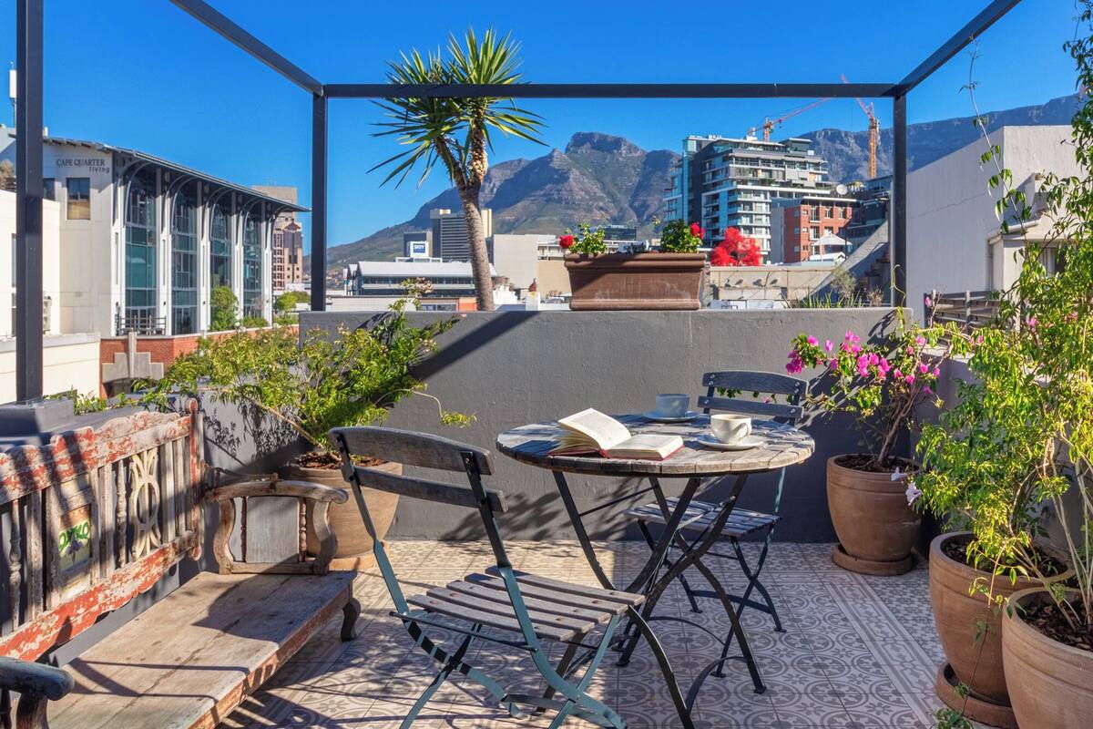 A rooftop terrace with a table, chairs, and potted plants.
