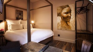 A bedroom with a four-poster bed, a desk with a remote control, and a wall-mounted artwork.