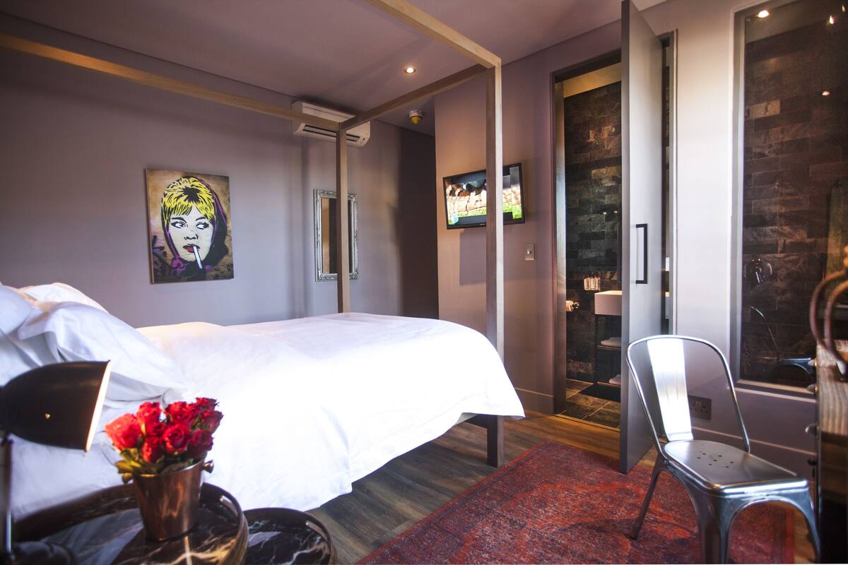 A modern hotel room with a large bed, a flat-screen TV, a mirror, and a red rug.