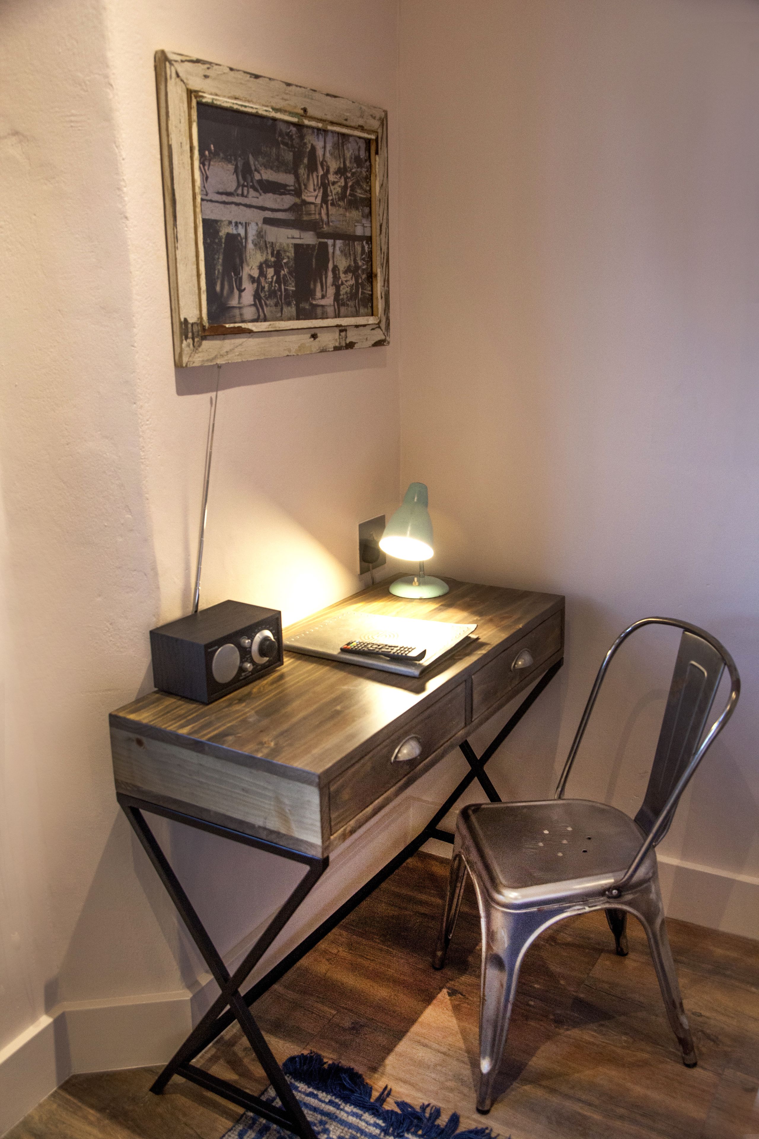 Escritorio en esquina con lámpara, radio y control remoto. Hay una silla frente al escritorio.