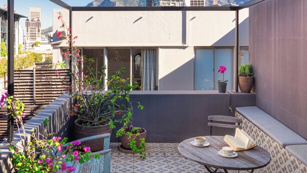 A rooftop patio with a round table, chairs, potted plants, and a view of the cityscape.