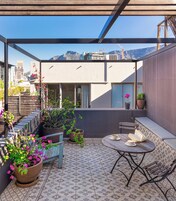 En takterrass med ett runt bord, stolar, krukväxter och utsikt över stadsbilden.