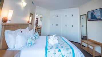 A hotel room with a bed, a wooden nightstand, a mirror, a wardrobe, and a television on the wall.