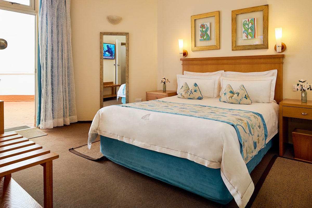 A hotel room with a bed, bedside tables, a mirror, and artwork on the wall.