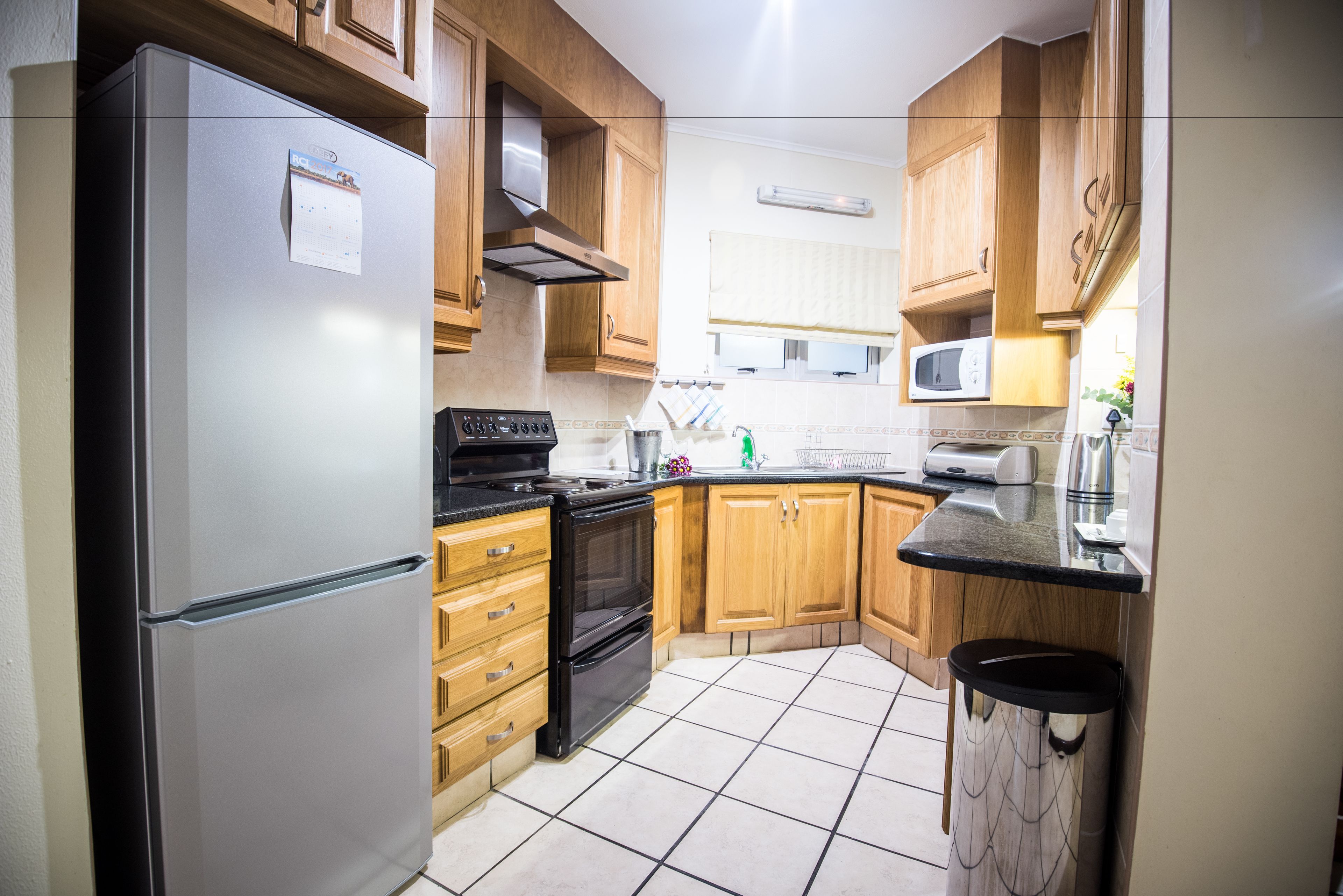 Una cocina con armarios de madera, un refrigerador de acero inoxidable, un horno negro y un microondas.