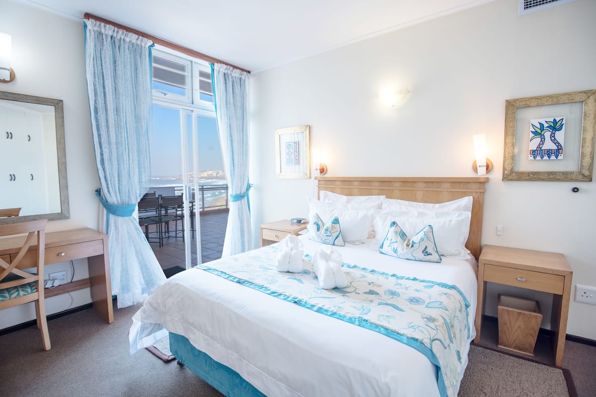 A hotel room with a bed, a desk, a chair, a window with curtains, and a balcony.
