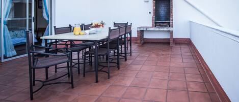 Une terrasse avec une table et des chaises, un barbecue et une porte-fenêtre coulissante.