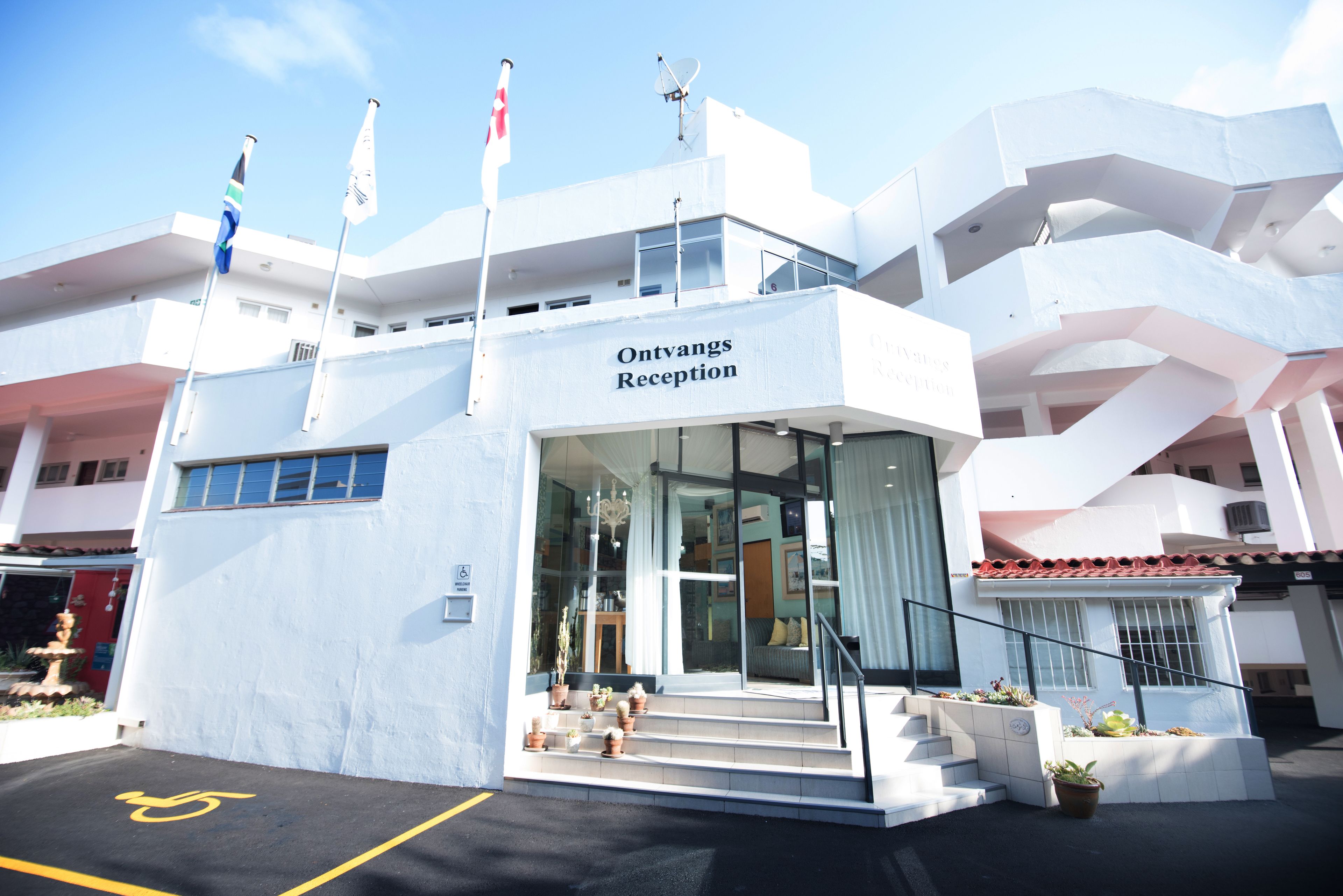 A modern building with a reception area, multiple flags, and a clear sky.