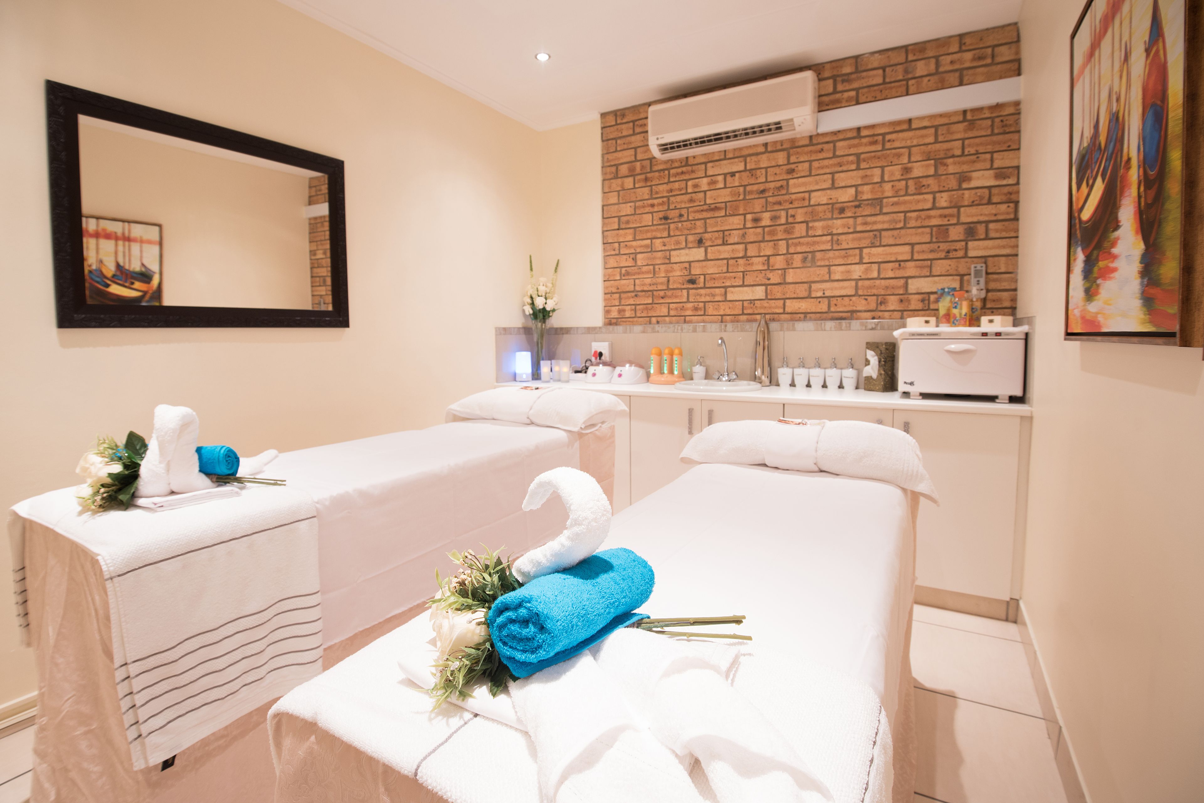 A spa room with two treatment beds, a mirror, a brick wall, and a sink area.