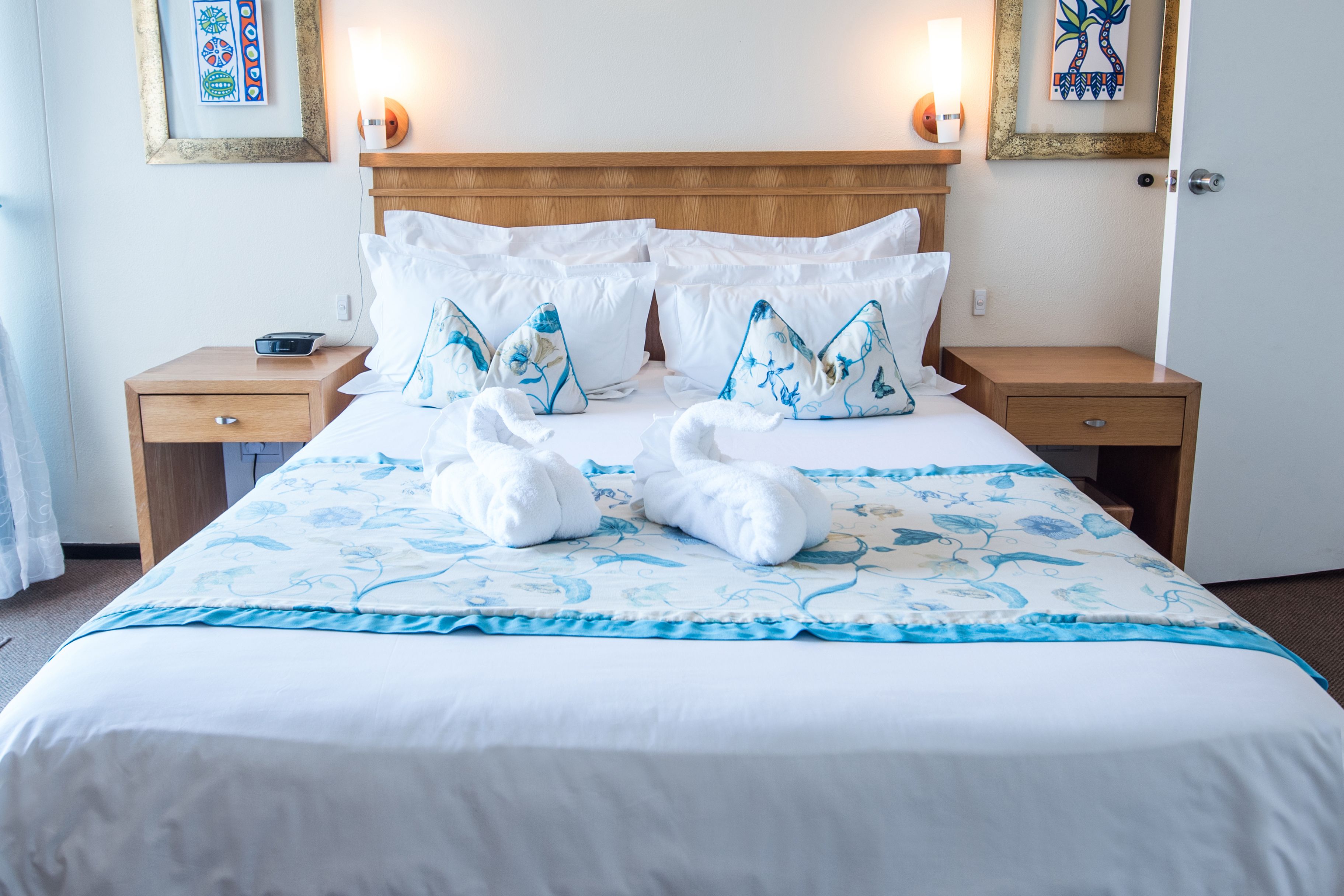 A neatly made bed with white and blue floral bedding, two nightstands with lamps, and framed artwork on the walls.