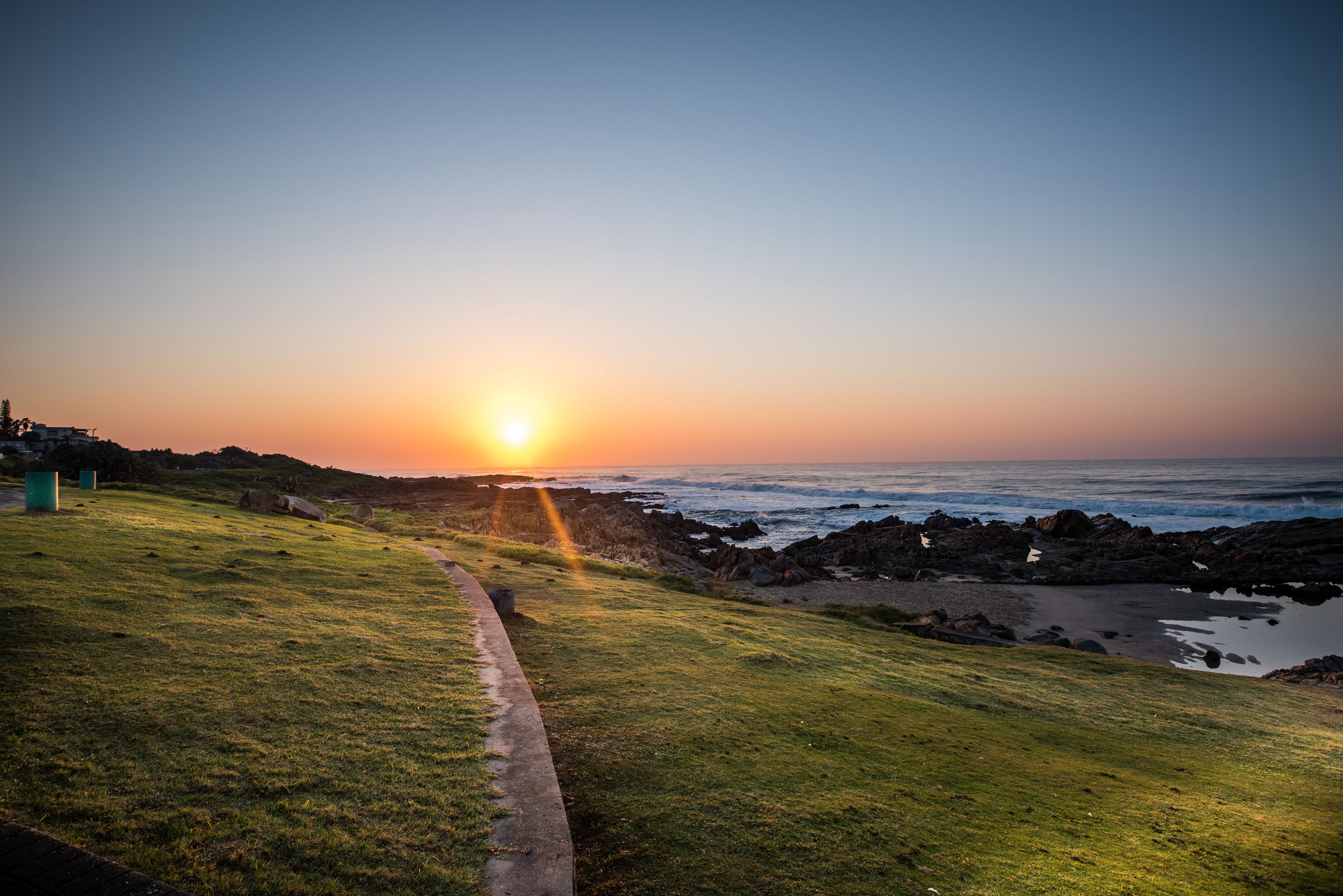 A coastal path leading to the ocean with a sunset in the background.
