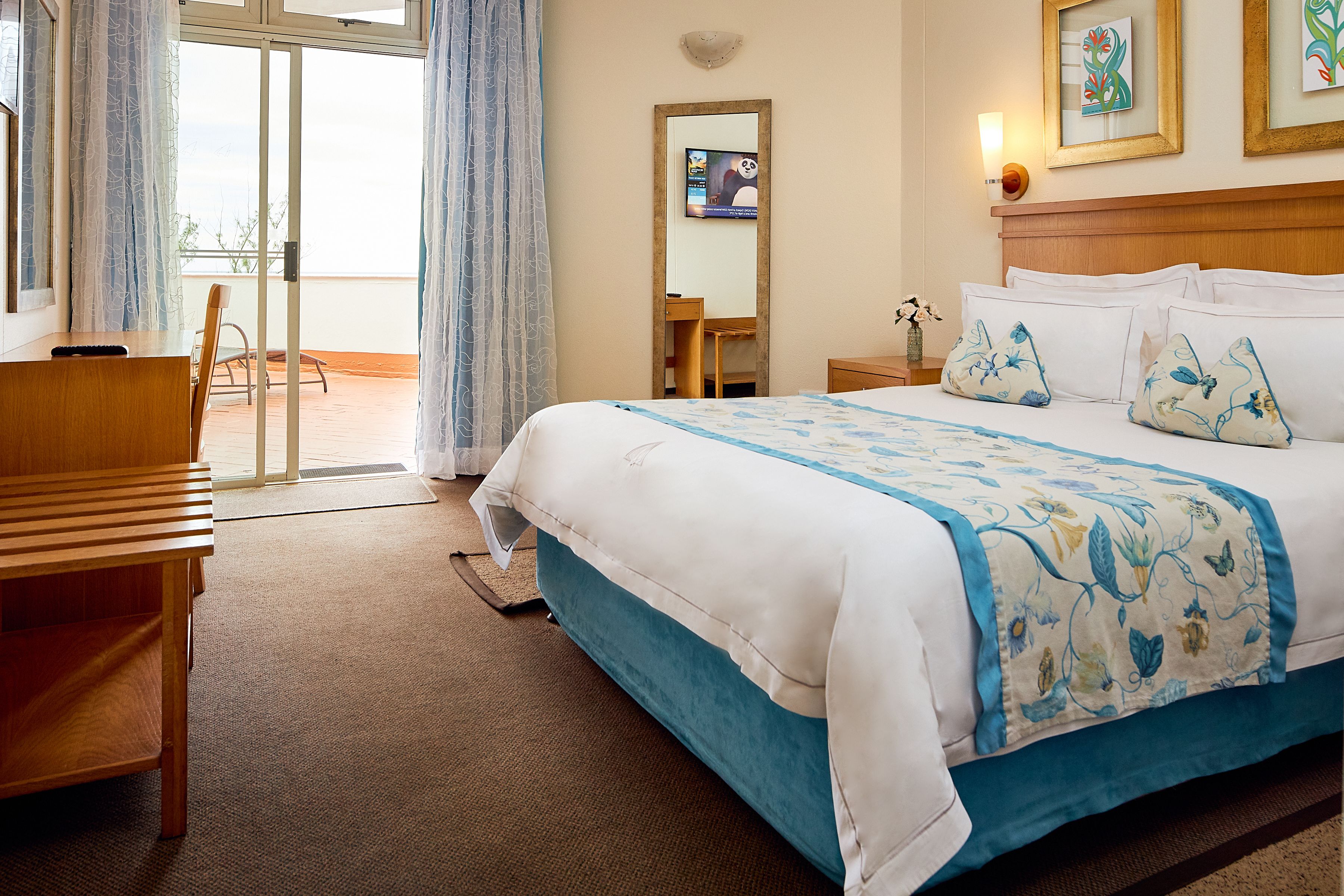 A hotel room with a bed, a desk, a chair, a small table, and a view through a sliding door.