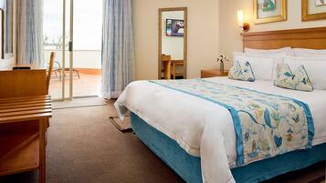 A hotel room with a bed, a desk, a chair, a small table, and a view through a sliding door.