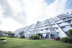 A modern multi-story building with a unique sloped design, featuring balconies and large windows.