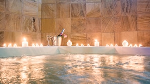 Un bain à remous avec des bougies et une bouteille de champagne, le tout entouré de murs en pierre.