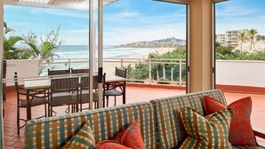 Un balcon avec un canapé et une table à manger, offrant une vue sur la plage et le paysage urbain.