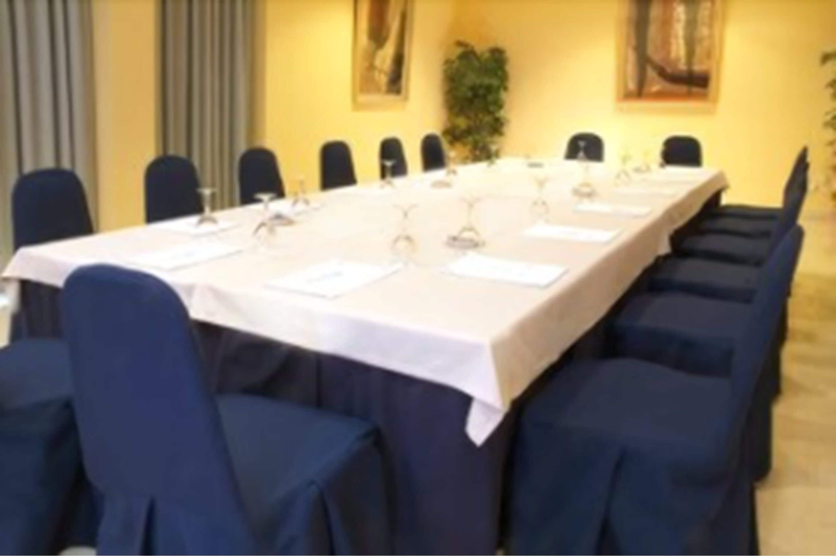 Una sala conferenze con un lungo tavolo, sedie e una tovaglia bianca.