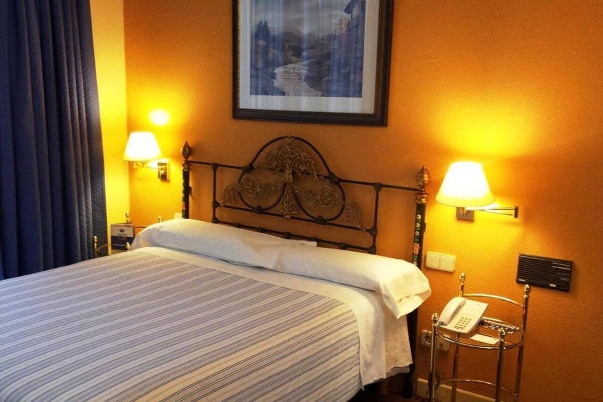 A hotel room with a bed, two bedside lamps, a telephone, and a framed picture on the wall.