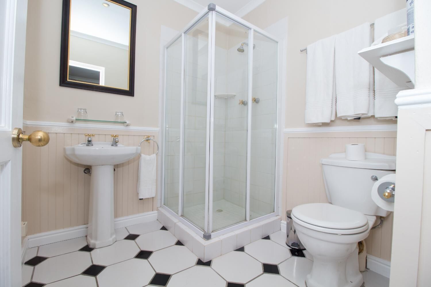 A bathroom with a glass shower enclosure, a pedestal sink, a toilet, and a mirror with a gold frame.