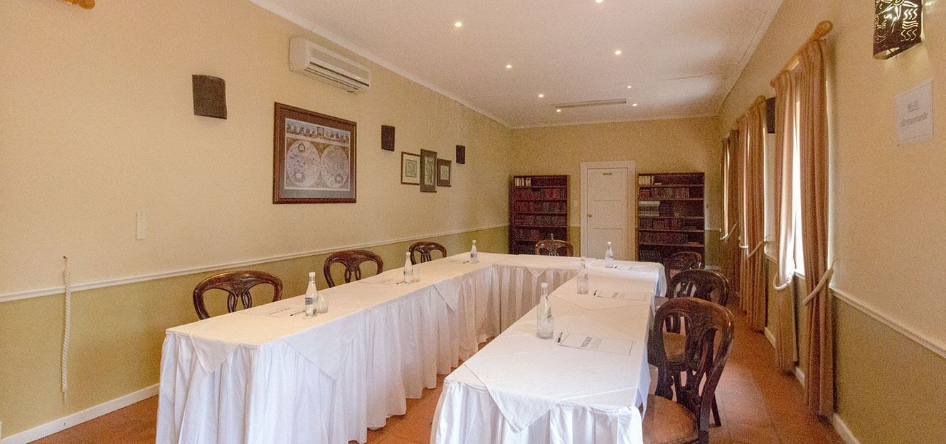Uma sala de conferências com mesas compridas, cadeiras e uma estante.