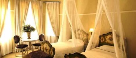Une chambre d’hôtel avec deux lits, un coin salon avec une table et des chaises, et une fenêtre avec des rideaux.