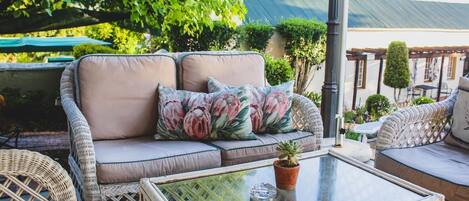 A wicker sofa with floral cushions, a glass coffee table with a potted plant, and outdoor furniture.
