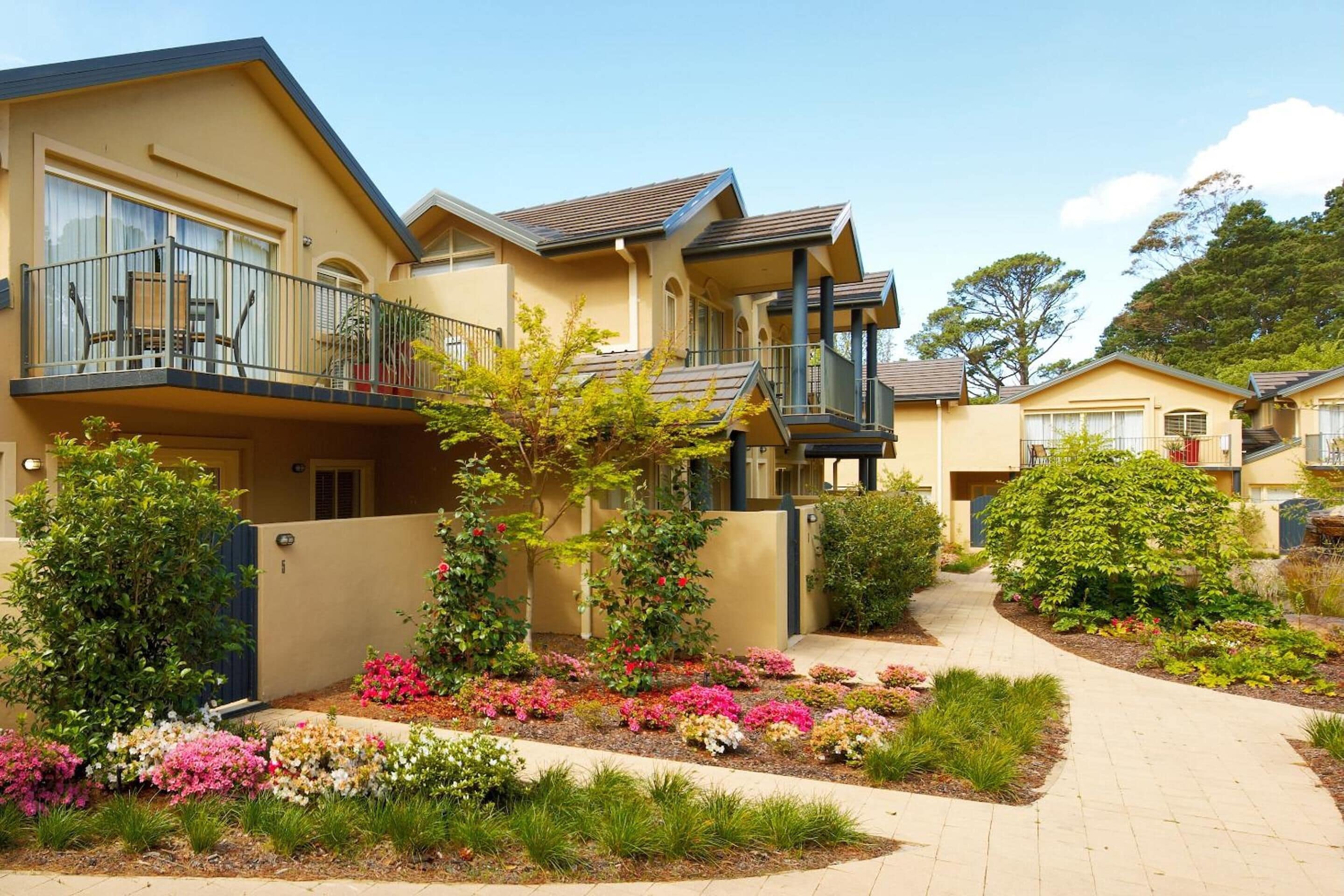A residential building with multiple balconies, a landscaped garden with various plants and flowers, and a paved walkway.